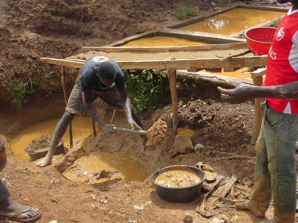 Miners work an open pit beneath a timber shelter